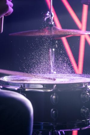 The Man Plays The Drums, On The Background Of Colored Lights